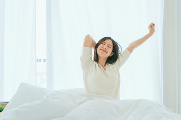 white dress asian beautiful woman stretching morning wake up bedroom with white curtain background...