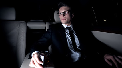Millionaire drinking glass of elite brandy on back seat of car, business trip