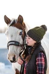 teenag girl holding her handsome horse.  Winter scene with snow in background