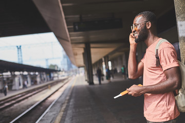 Fototapeta premium Afro-american man standing on station and using mobile phone