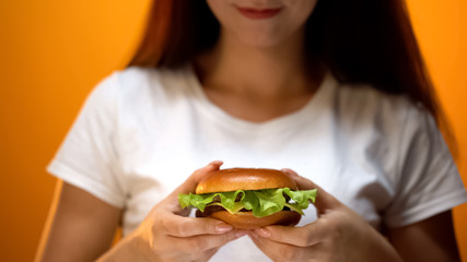 Girl holding home-made burger with lettuce inside, delicious snack, close up