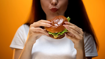 Lady chewing hamburger, high calorie nutrition, risk of gastritis, problem