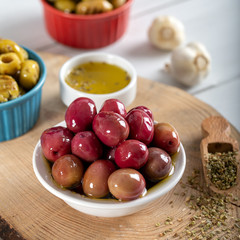 Green and red olives in bowl with olive oil and spices on wooden background