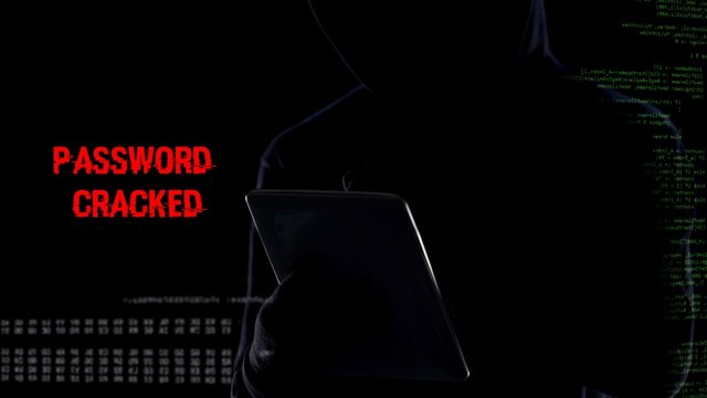 Male in hood typing on tablet, cracking password, gathering personal data
