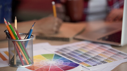 Female designers taking notes, colored pencils holder standing on color spectrum