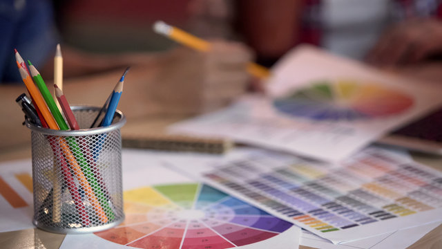 Colored pencils standing in metal holder, designers looking at color spectrum