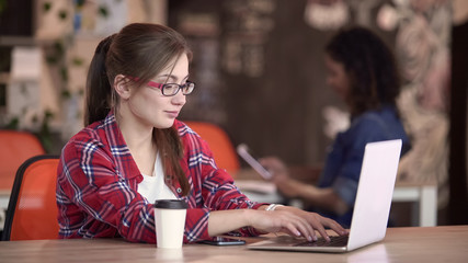 Female journalist in eyeglasses sitting in cafe and typing on laptop, freelance