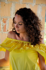 young happy curly dark-haired girl in a yellow dress with bare shoulders