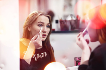 A young girl does make-up in a beauty salon. The girl in front of the mirror is making up. Beauty saloon.