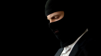 Male in balaclava feeling guilty about crime, isolated on black background