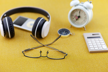 Headphone with white alarm clock,compass and calculator on gold glitter texture sparkling shiny paper background