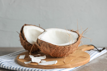 Cutting board with split coconut on table against grey background