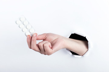 Female hand out of the hole in the paperman, holding blisters with pills. Isolate on white background.