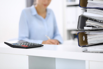 Calculator and binders with papers are waiting to be processed by business woman or bookkeeper back...