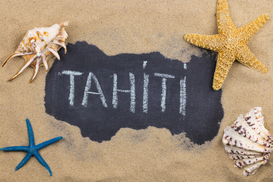 Handwritten word TAHITI written in chalk, among seashells and starfishes.