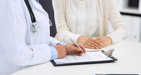 Unknown woman doctor and  female patient  discussing something while standing near reception desk in emergency hospital. Physician at work in clinic. Medicine and health care concept