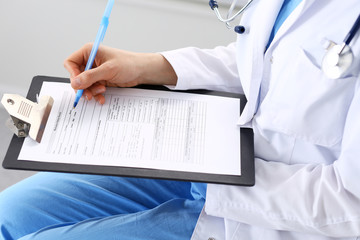 Woman doctor at work at hospital. Young female physician write prescription or filling up medical form while sitting in hospital office, close-up