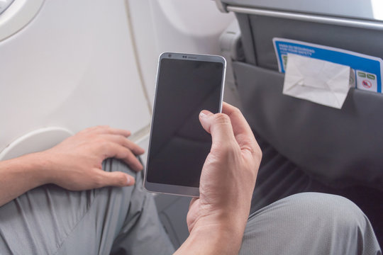 Male Hands Holding A New Smart Phone On An Airplane, Turning On Or Off At Take Off Or Landing / Young Man In A Bussines Or Vacations Trip Using A Mobile Device For Communication, To Stay Connected