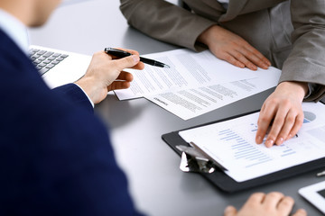 Business people and lawyer discussing contract papers sitting at the table, hands close-up. Teamwork or group operations concept