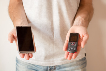 Male hands holding a new smart phone and an old cellphone, on white background. Planned...