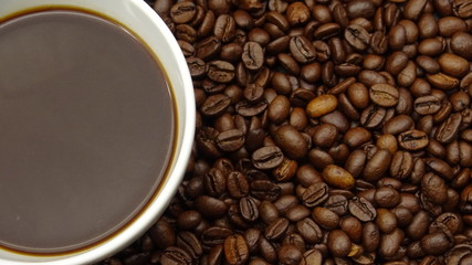 A cup of black coffee over roasted coffee beans