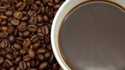 A cup of black coffee over roasted coffee beans