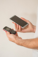 Male hands holding a new smart phone and an old cellphone, on white background. Planned obsolescence concept, technology development, history of communications, millenial devices