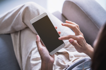 Young woman siiting on sofa and using smart phone at home