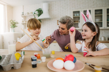 Gray-haired woman helping a boy with painting eggs at home