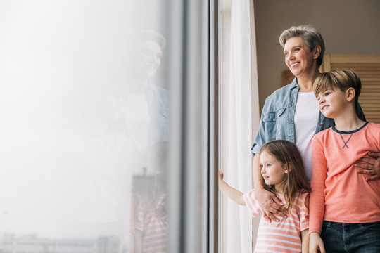 Waist up photo of smiling granny and her grandchidren at window