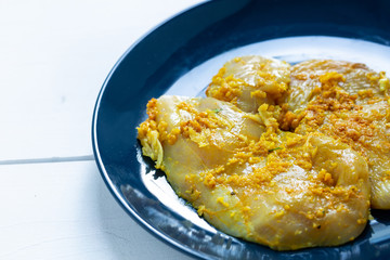 Raw, flavored with turmeric, basil and oregano chicken fillet on a plate.