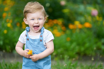 Portrait of a one-year-old girl with blue eyes holding an orange flower and laughing