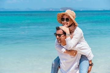 Fototapeta na wymiar Young happy muslim couple white dress on seashore. Travel Vacation Retirement Lifestyle Concept. Man giving piggyback ride to girlfriend on the beach on the beach in vacation day. summer time.