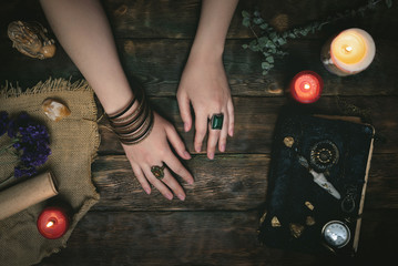 Enchantress female hands and an ancient magic book in the light of burning candle on a wooden table...