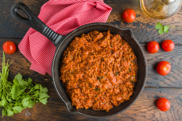 Bolognese sauce with minced meat and tomatoes in black pan on wooden rustic table, horizontal view...