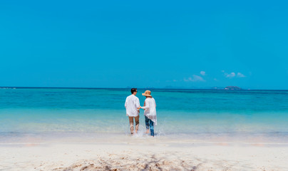 Young happy couple white dress on seashore. Travel Vacation Retirement Lifestyle Concept. young couple holding hands and turn back on the beach in vacation day. summer time.