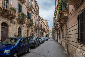 Naklejka premium Typical italian narrow street with cars in the row in the island of Ortigia, Syracuse, Sicily, Italy