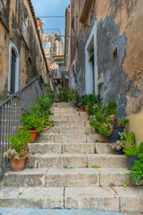 Fototapeta na wymiar Narrow street with greenery in flower pots on the floor in Ragusa, Sicily, Italy