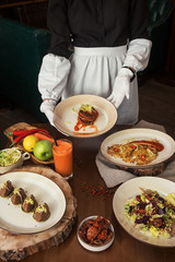 Healthy vegeterian food on brown wood board. The waitress brings food. Salad from beet with dried tomatoes and cabbage, potato vegan pancakes, dried tomatoes, pate from red beans, baked vegetables in