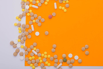 Medical colorful pills, capsules or supplements for the treatment and health care on orange and white background. Creative idea. Drugs. Sad. Die. Illness.