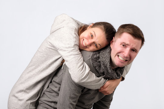 Smiling Couple Embracing In Piggy Back And Looking At Camera On White Background