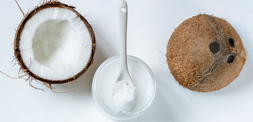 Coconut oil in a jar and coconut halves on the table on a white background