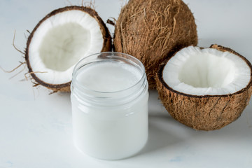 Coconut oil in a jar and coconut halves on the table on a white background