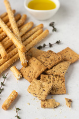 Italian grissini or salted bread sticks and multigrain crackers on a light stone background. Copy space. 