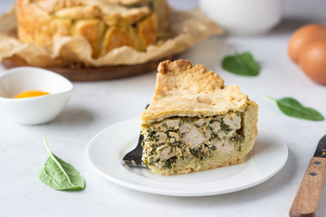 Spinach, chicken and ricotta pie with fresh spinach leaves, ricotta and eggs on a light stone background.