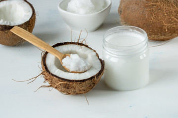 Coconut oil in a jar and coconut halves on the table on a white background