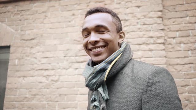 Portrait shot of handsome smiling, winking and saying yes African American man in a coat and a scarf. Handheld slow motion shot