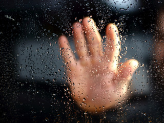 Obraz na płótnie Canvas Male hand palm silhouette through behind the window with raindrops reaching for the glass. A request for help, depression blurred bokeh background. Refusal denial of alcohol and drugs