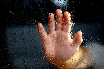 Fototapeta premium Male hand palm silhouette through the window with raindrops reaching for the glass. A request for help, depression blurred bokeh background