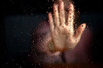 Female hand palm silhouette outside the window with raindrops reaching for the glass. A request for...